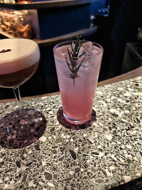 Espresso Martini und rosafarbener Longdrink mit Rosmarinzweig auf der Terrazzoplatte des Tresens