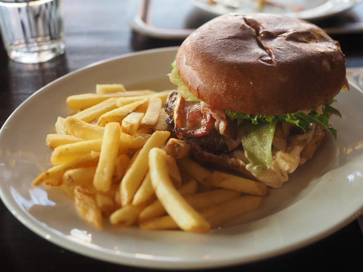 Burger mit Rindfleisch, Speck und Salat im Briochebrötchen, daneben Pommes frites