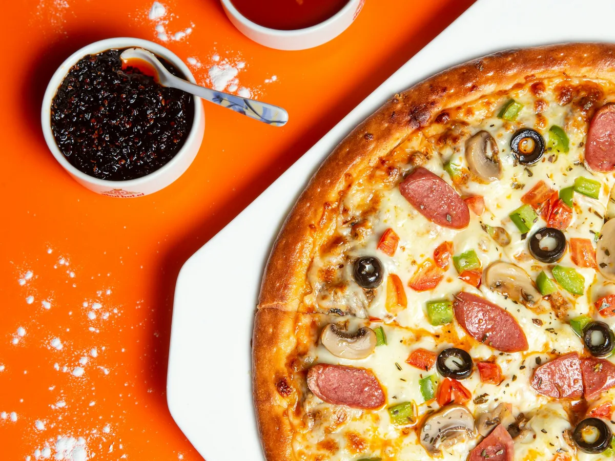 Pizza mit Peperoni und Käse auf orangefarbenem Untergrund