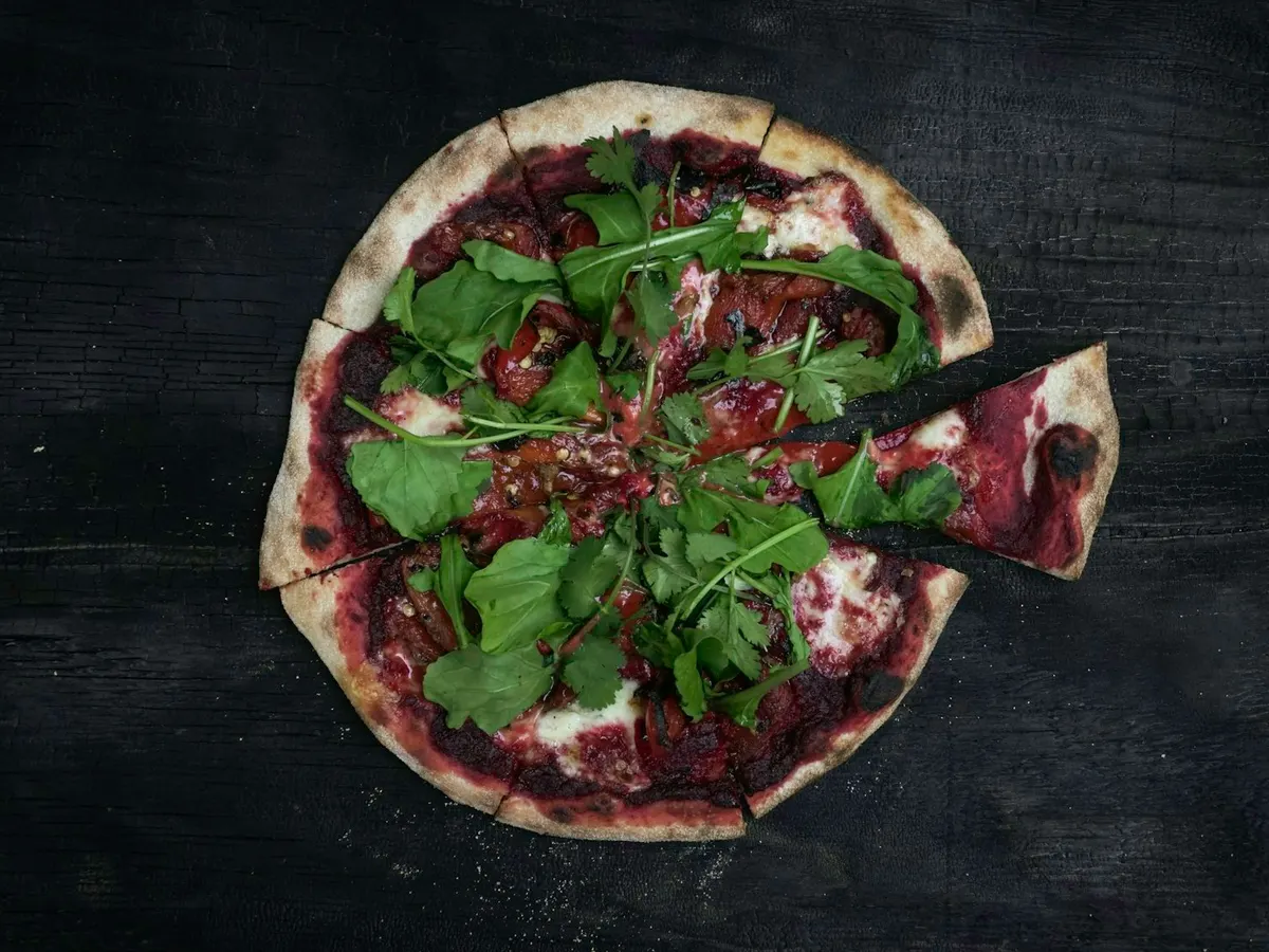 Pizza mit Grünzeug und Fleisch auf einem Holztisch