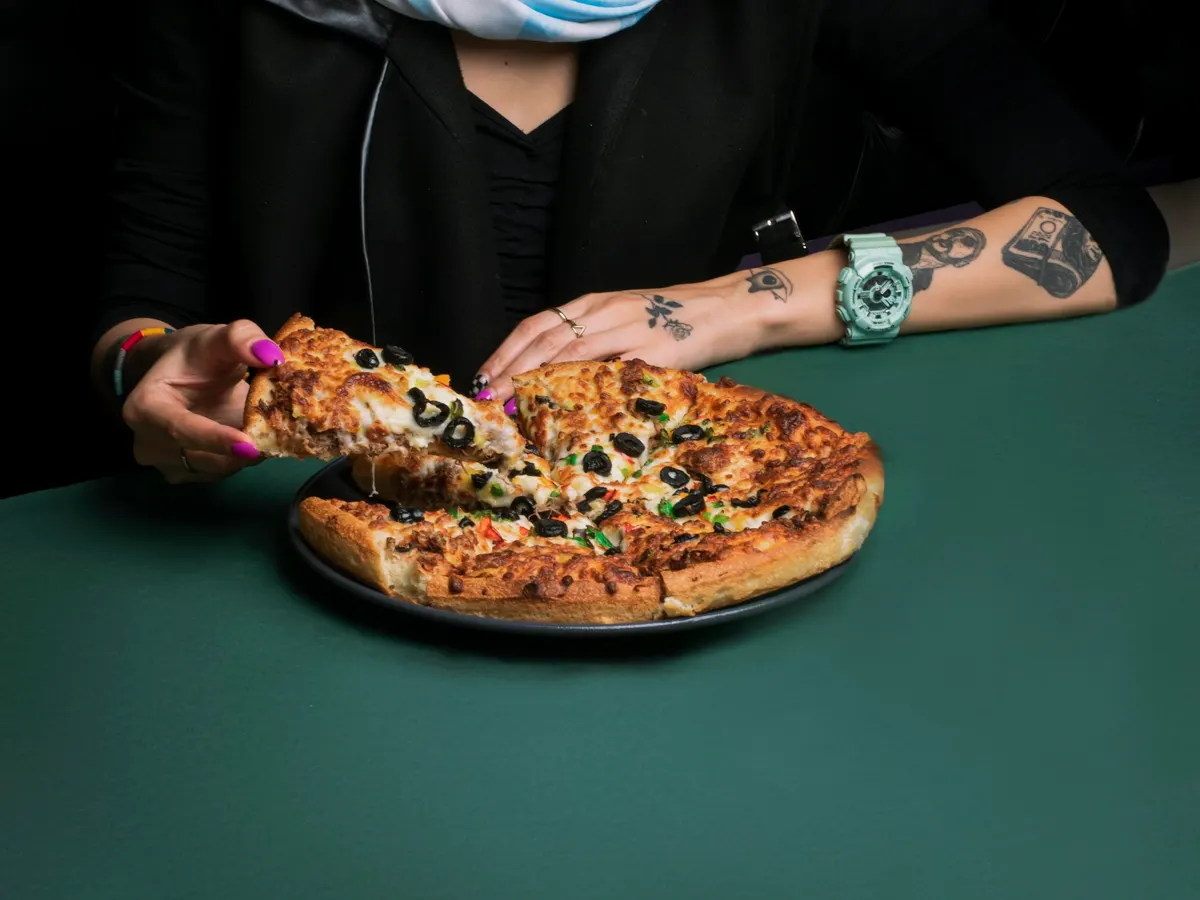 Person isst ein Stück Pizza vom Teller