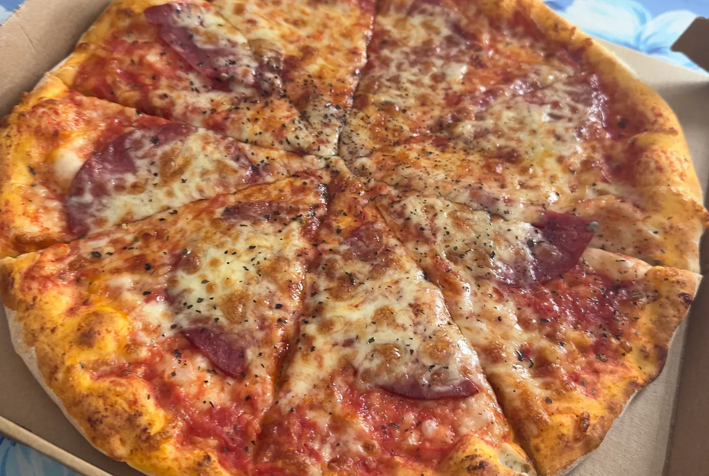 Ganze Salamipizza mit geschmolzenem Käse und Oregano in einem Pizzakarton