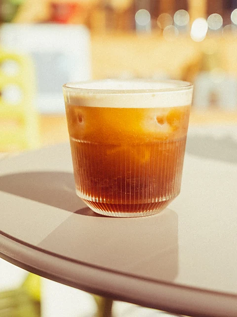 Glas Nitro Cold Brew mit cremiger Schaumkrone auf einem runden Tisch im Gegenlicht