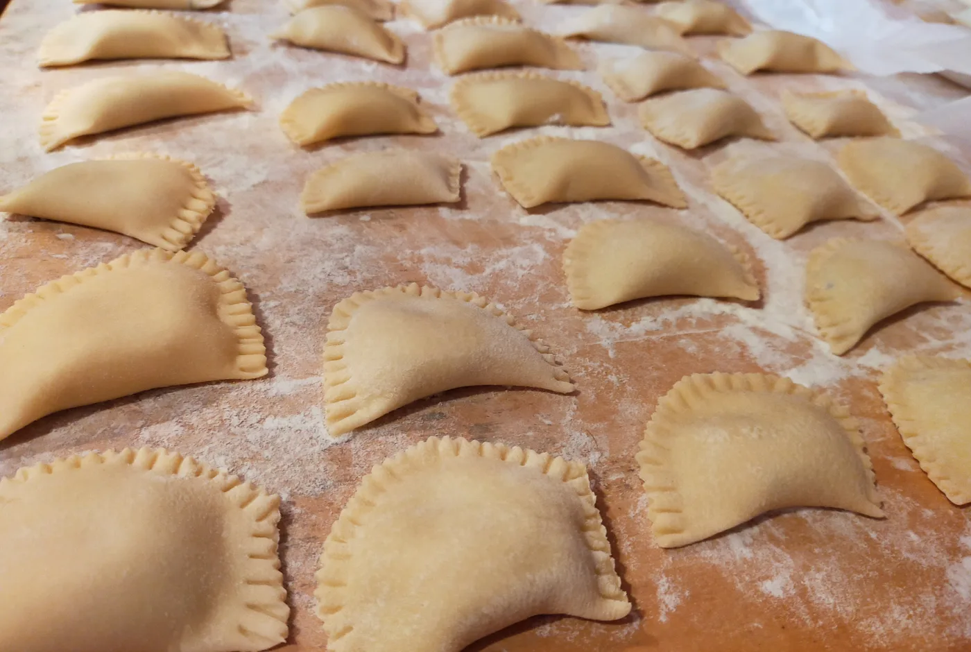 Frisch geformte Ravioli in Reihen auf einem bemehlten Holzbrett