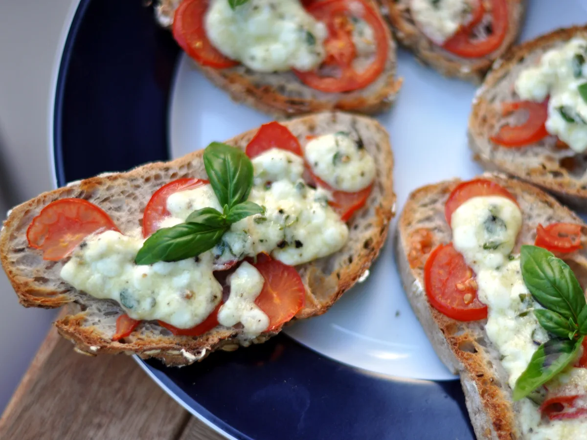 Geröstete Brotscheiben mit Tomaten, Mozzarella und Basilikum auf einem Teller