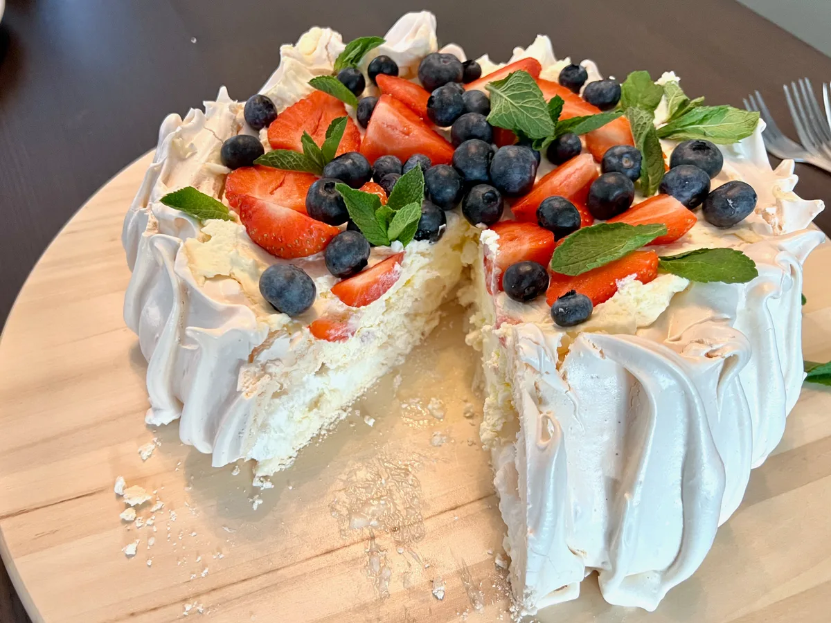 Angeschnittene Pavlova aus Baiser mit Sahne, Erdbeeren, Blaubeeren und Minze