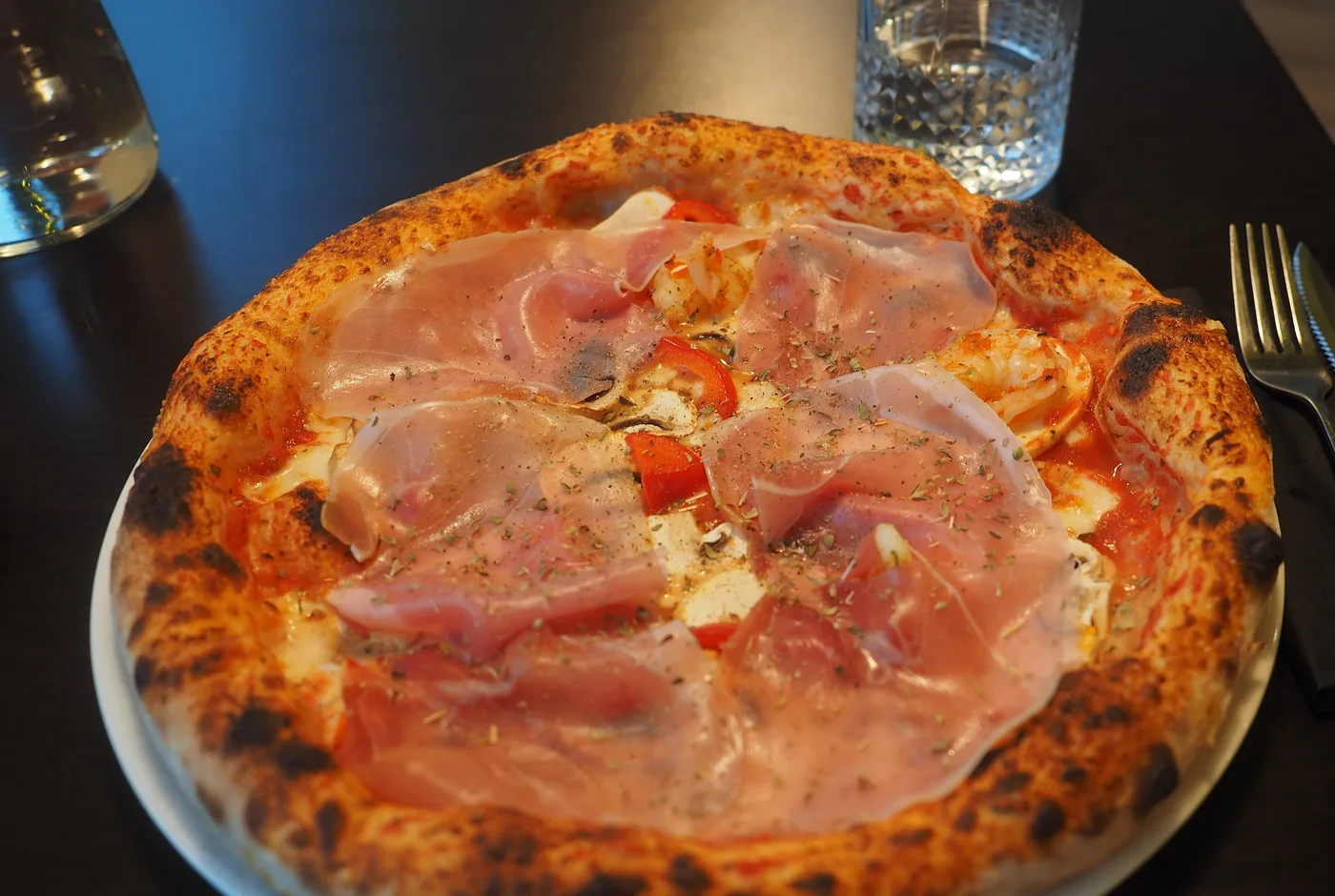Pizza mit rohem Schinken und hohem Rand auf einem weißen Teller