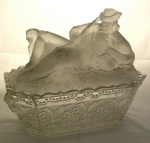 Deckeldose aus mattiertem Pressglas, auf dem Deckel die Figur eines liegenden Mannes mit Hut, der Korpus mit Blumenrelie
