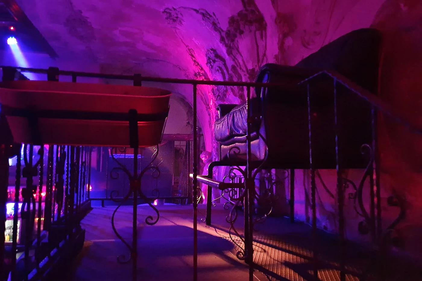 Empore der Prinzenbar mit schmiedeeisernem Geländer, roten Bänken und Stuckdecke im violetten Licht