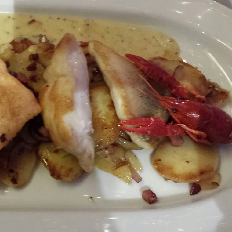 Gebratenes Fischfilet und Flusskrebs auf Bratkartoffeln in heller Sauce