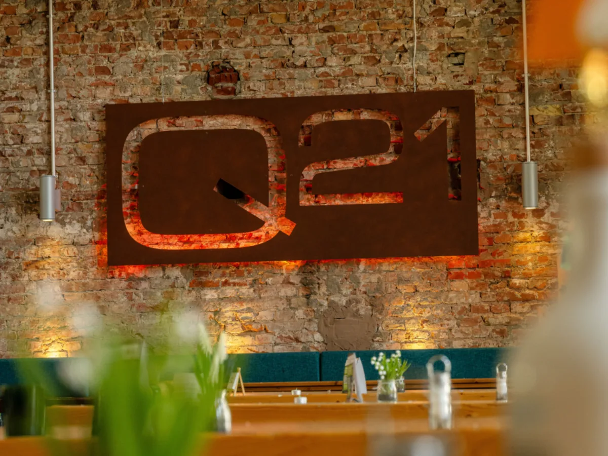 Q21-Schriftzug aus Metall an einer Backsteinwand im Gastraum
