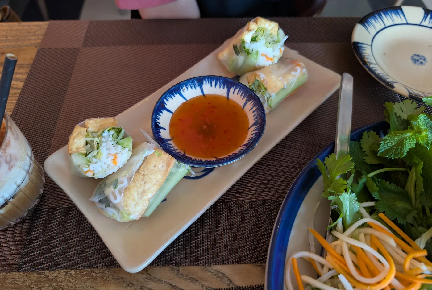 Aufgeschnittene Sommerrollen mit Tofu, Reisnudeln und Salat neben einer Schale Chilisauce