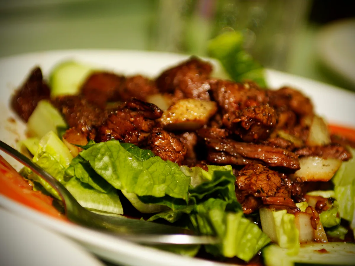 Gebratene Rindfleischstücke mit Pfeffersoße auf Salat und Gurken in einer weißen Schale