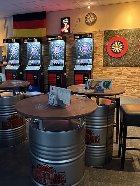 Stehtische aus Metallfässern vor Dartautomaten und Dartscheiben, an der Wand eine Deutschlandfahne