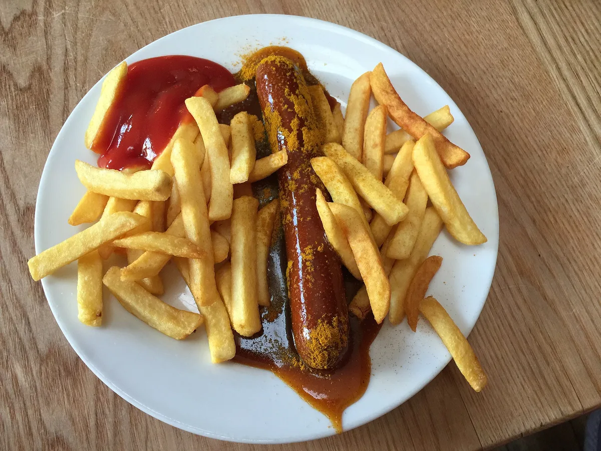 Currywurst mit Currypulver, Sauce, Pommes frites und Ketchup auf einem weißen Teller