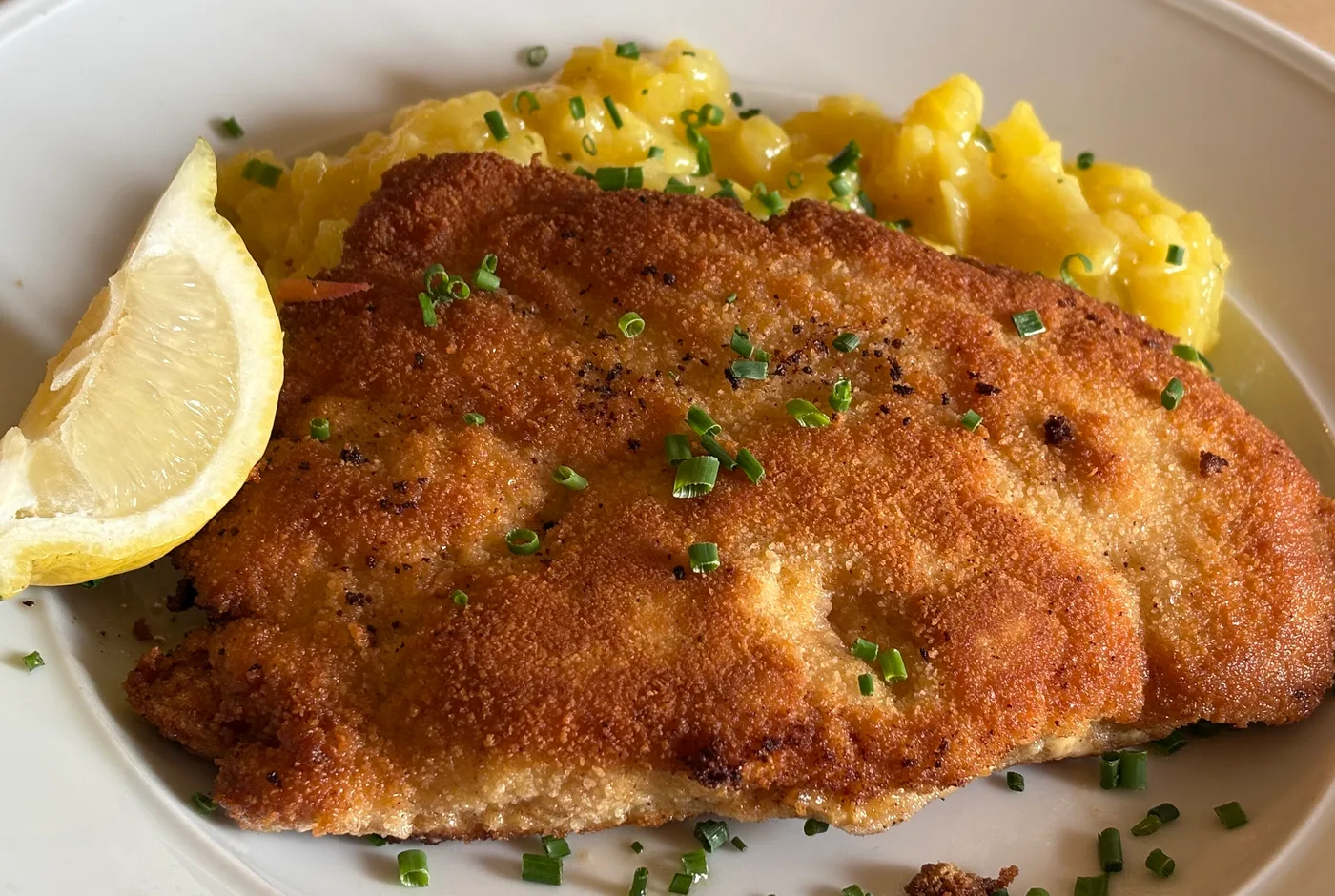 Goldbraun paniertes Cordon Bleu mit Kartoffelsalat, Schnittlauch und Zitronenspalte auf einem weißen Teller