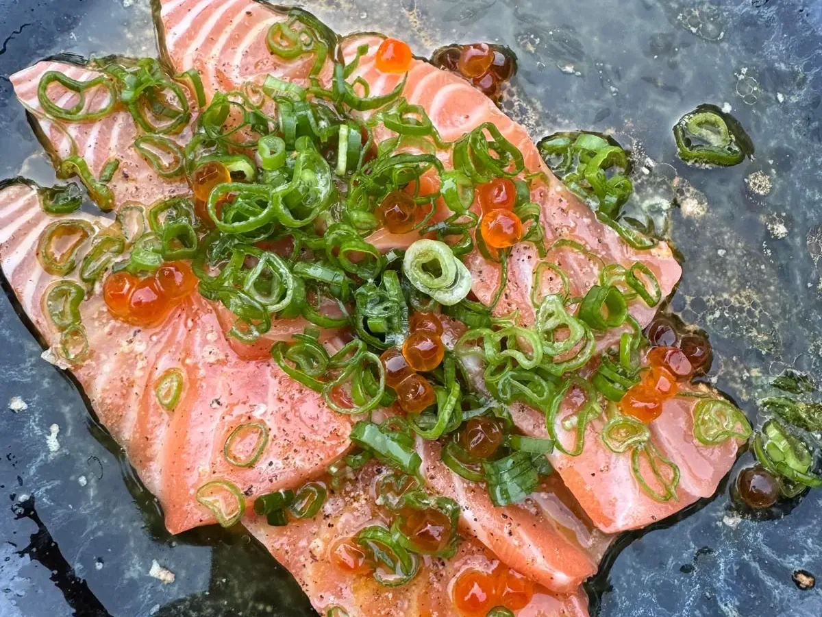 Gebeizter Lachs mit Lachskaviar und Frühlingszwiebeln auf blauem Teller