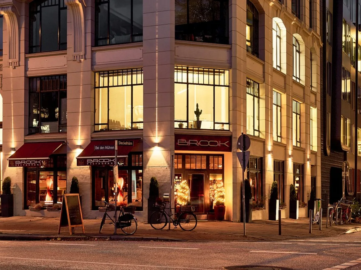 Beleuchtete Außenfassade des Restaurant Brook am Abend mit roter Markise