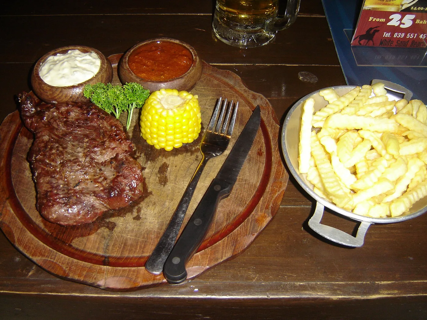 Rumpsteak auf einem Holzbrett mit Maiskolben, Saucen und Pommes