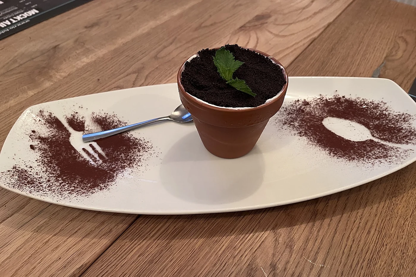 Dessert in einem Tontöpfchen mit Schokoladenstreuseln und Minze auf einem länglichen Teller