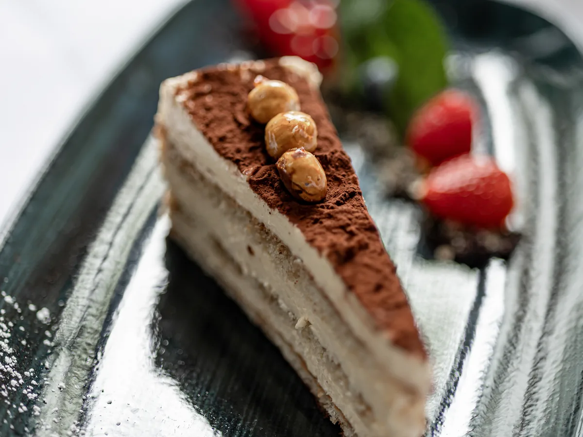 Stück Tiramisu mit Kakao und Erdbeere auf dunklem Teller