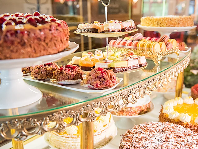 Tortentheke mit Beerentorte, Törtchen auf Etageren, Macarons und Kuchen auf goldenen Ständern