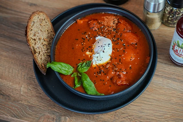 Shakshuka in schwarzer Schale mit pochiertem Ei, Basilikum und einer Scheibe geröstetem Brot