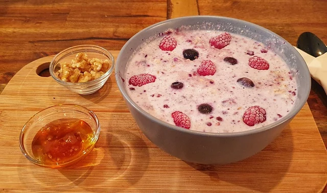 Beeren-Porridge in einer grauen Schale, daneben Walnüsse und Honig