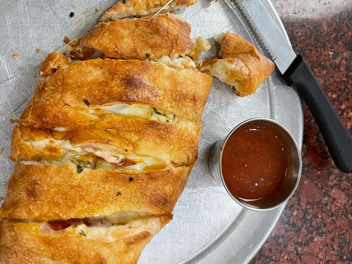 Aufgeschnittene Calzone mit geschmolzenem Käse, daneben ein Schälchen Tomatensauce