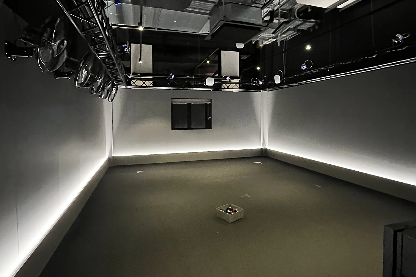 Leerer Spielraum mit hellen Wänden, LED-Lichtleisten am Boden und Motion-Capture-Kameras an einer Traverse unter der Decke