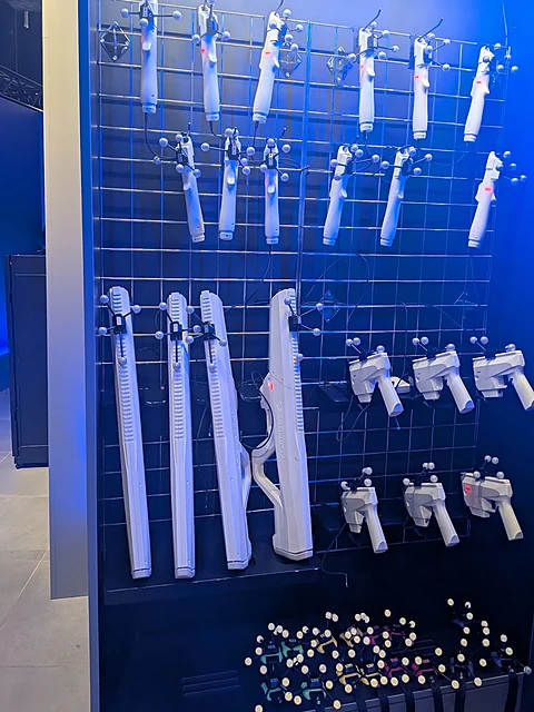 Wand mit aufgehängten weißen VR-Requisiten in Waffenform und Controllern vor blauem Licht