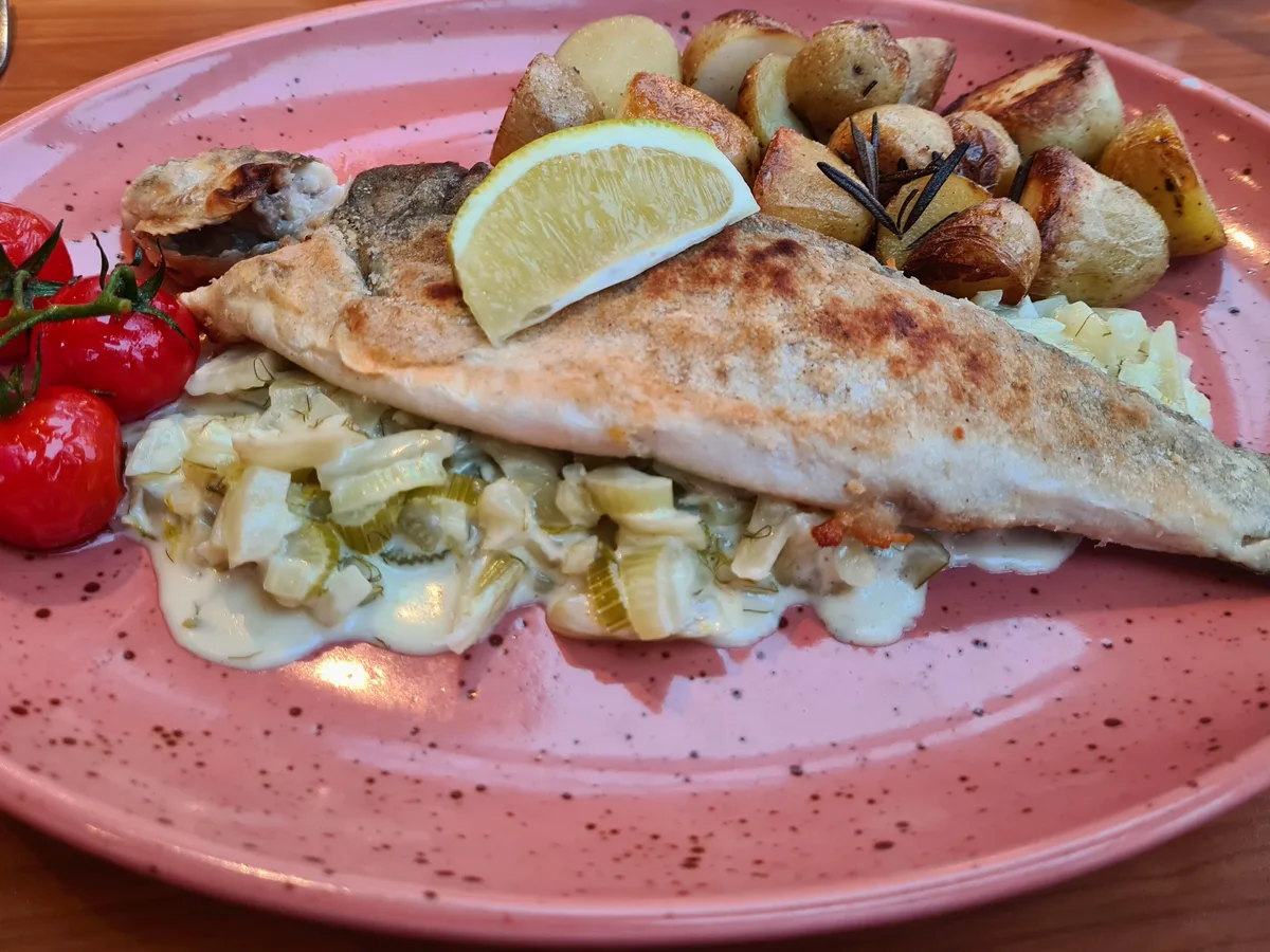 Gebratenes Fischfilet mit Zitrone, Bratkartoffeln und Tomaten auf einem Teller