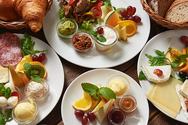 Frühstückstisch von oben mit Tellern voller Käse, Wurst, Obst, Dips und Croissants