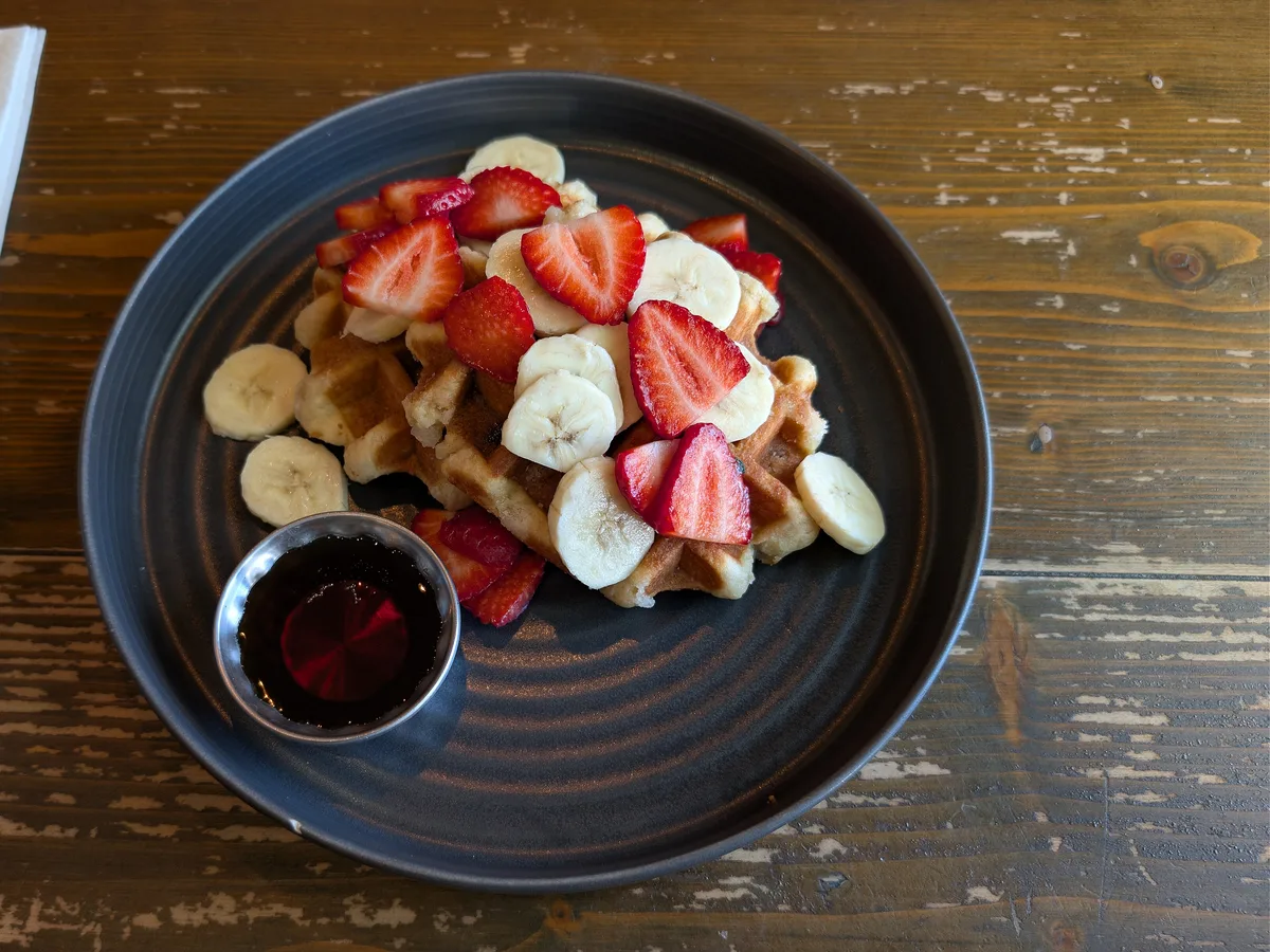 Waffel mit Erdbeeren und Bananenscheiben auf einem dunklen Teller