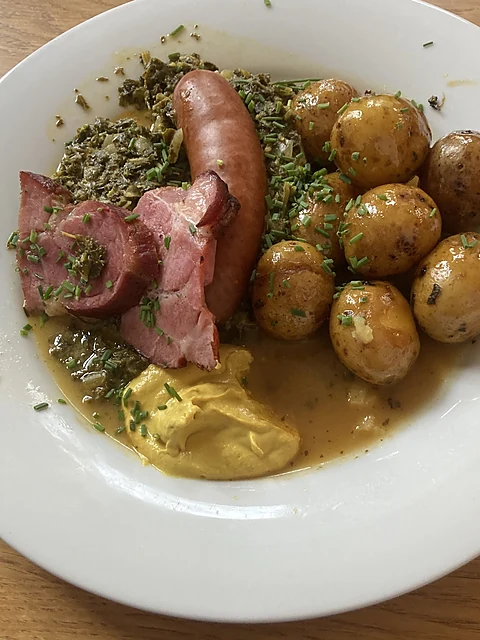 Teller mit Grünkohl, Kasseler, Kohlwurst, Bratkartoffeln und Senf auf Holztisch