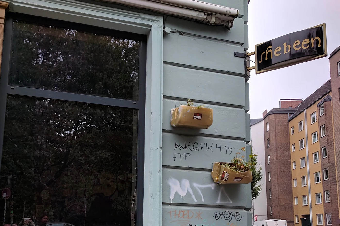 Ecke der Hein-Hoyer-Straße mit dem Messingschild shebeen über dem Eingang und Blumenkästen an der Wand