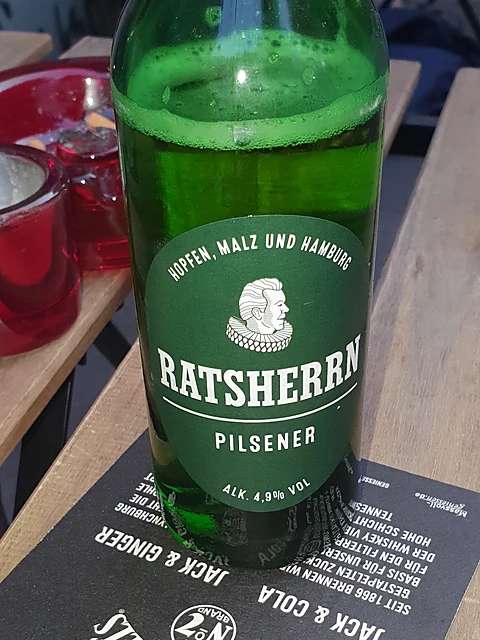 Flasche Ratsherrn Pilsener auf einem Holztisch vor der Kneipe, daneben ein roter Aschenbecher