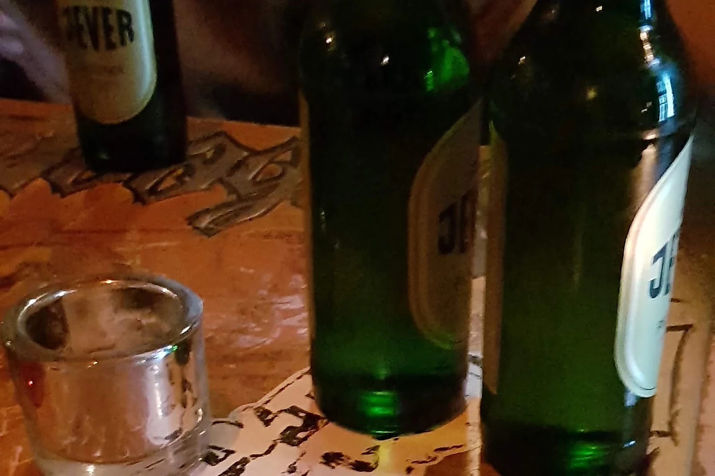 Drei Jever-Flaschen und ein Teelichtglas auf einem zerkratzten Holztisch im Shebeen
