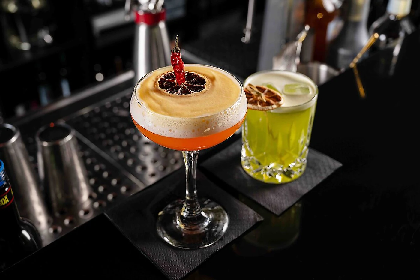 Zwei Cocktails auf schwarzen Servietten am Tresen der Skyline Bar, dahinter Barwerkzeug und Flaschen