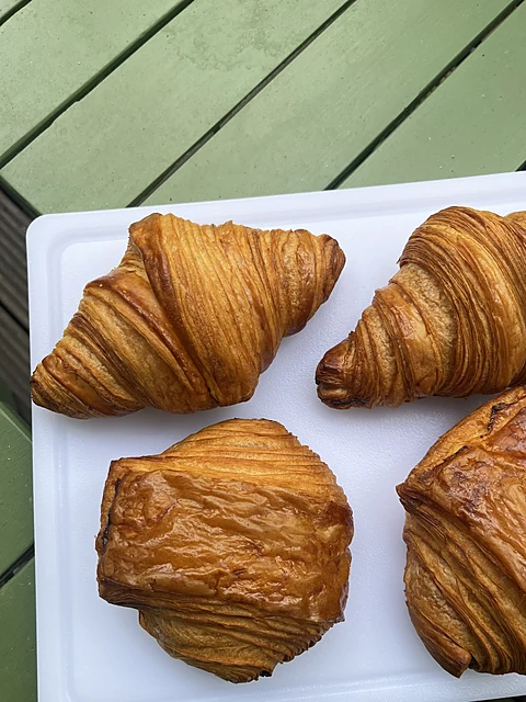 Vier goldbraune Croissants und Plunderstücke auf einem weißen Tablett auf einem grünen Holztisch
