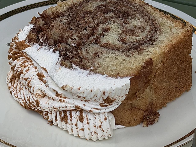 Dickes Stück Zimt-Rührkuchen mit Sahnehaube und Kakaostaub auf einem weißen Teller mit Goldrand