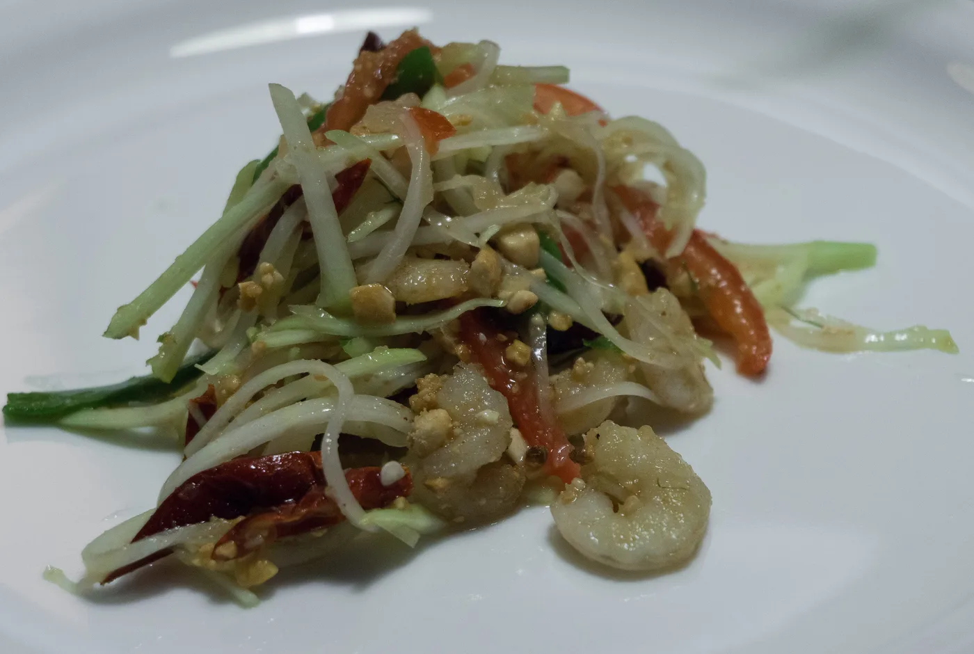 Grüner Papayasalat mit Garnelen, Chilischoten, Tomaten und Erdnüssen auf einem weißen Teller