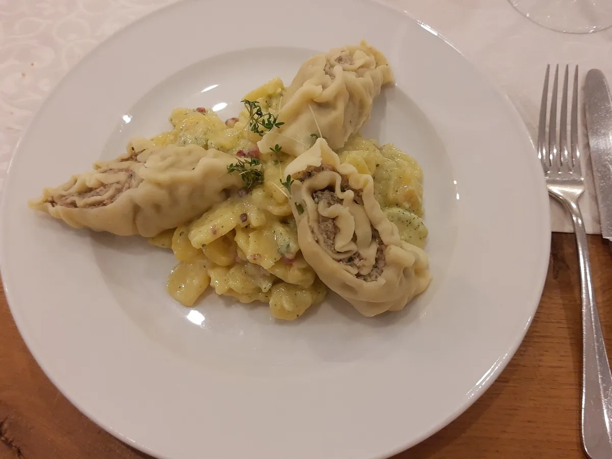 Maultaschen mit Spätzle und heller Sauce auf einem weißen Teller