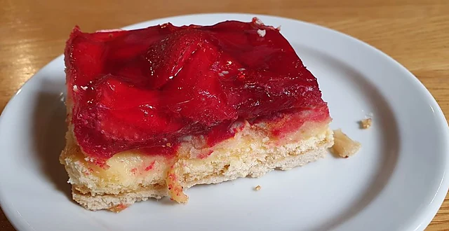 Ein Stück Erdbeerkuchen mit roter Glasur auf Mürbeteig auf einem weißen Teller