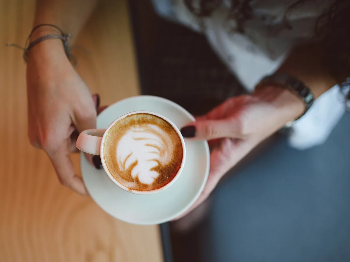 Tasse Cappuccino mit Milchschaum-Muster in zwei Händen