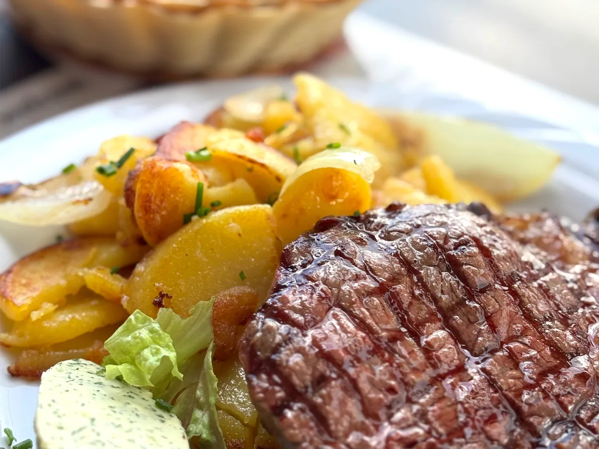Steak mit Bratkartoffeln, Kräuterbutter und Salat auf weißem Teller