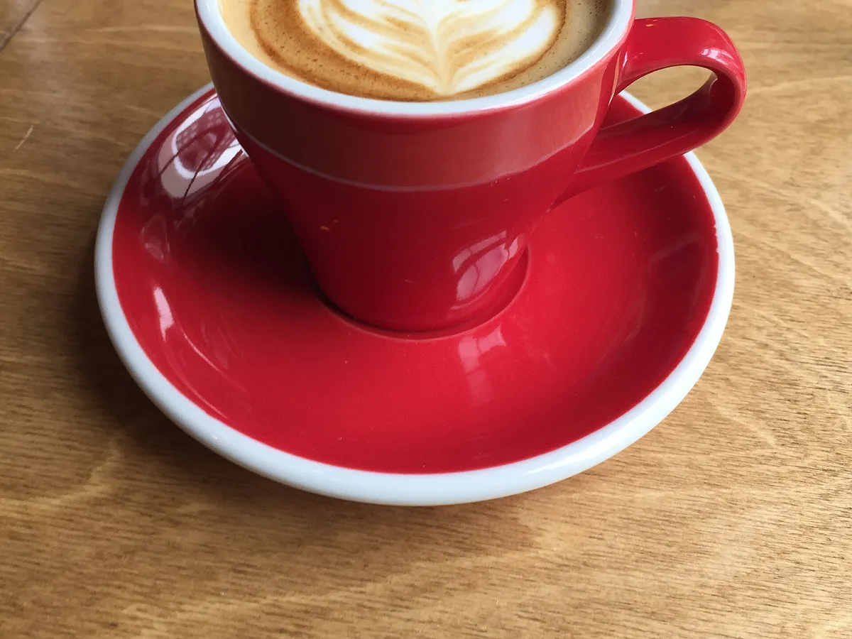 Cappuccino mit Milchschaummuster in einer roten Tasse auf Untertasse
