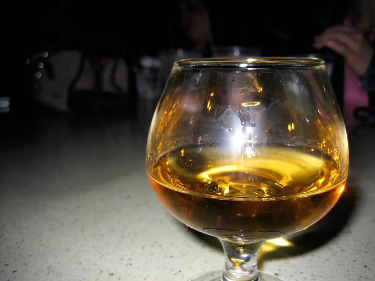 Glas mit bernsteinfarbenem Whisky auf einem Tresen in gedämpftem Licht