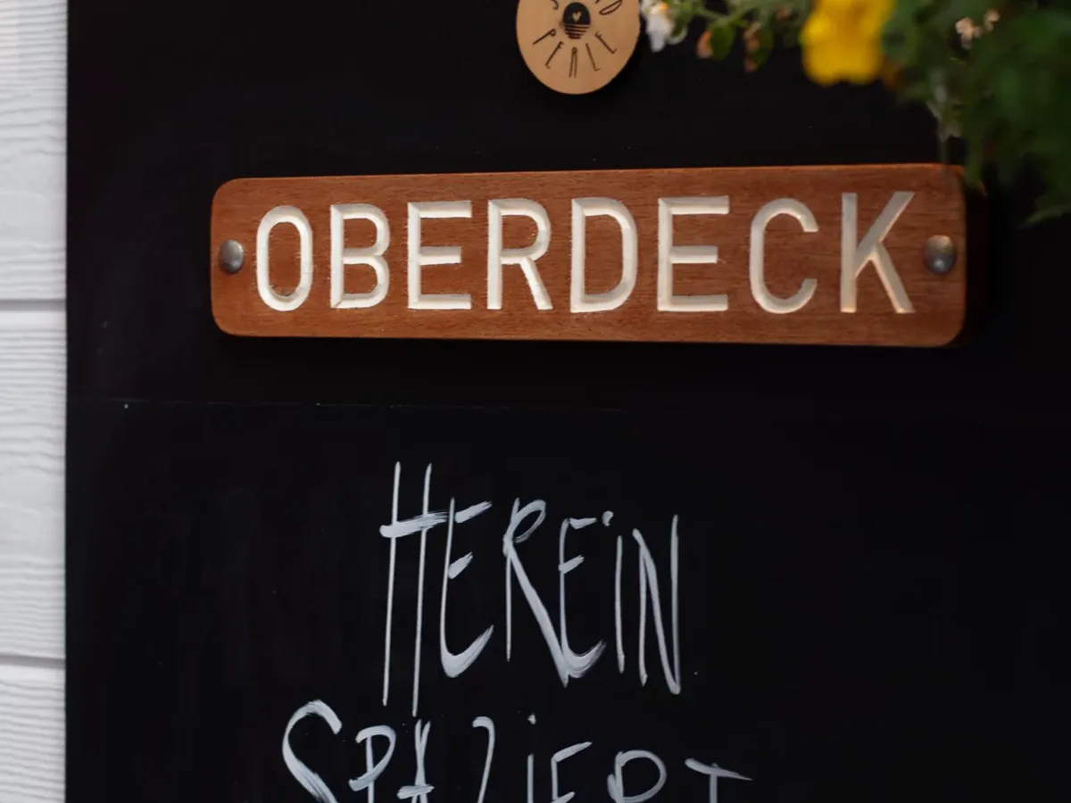 Tafel mit der Aufschrift Oberdeck, herein spaziert, daneben Blumen