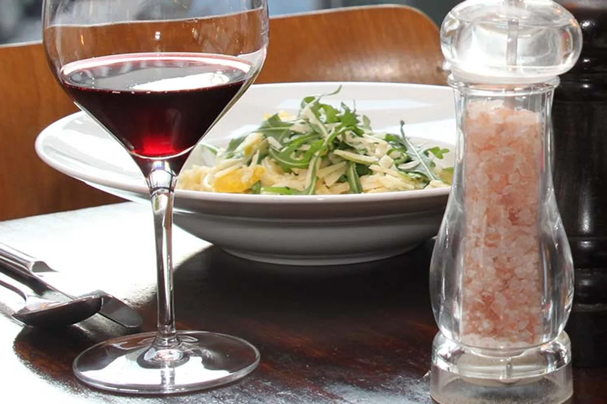 Schale mit Bandnudeln, Rucola und Parmesanhobeln, daneben ein Glas Rotwein